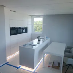 Nowoczesna, minimalistyczna kuchnia z białymi frontami i wyspą, w trakcie montażu; podłoga zabezpieczona folią i taśmą malarską, widoczne kartony i akcesoria montażowe.