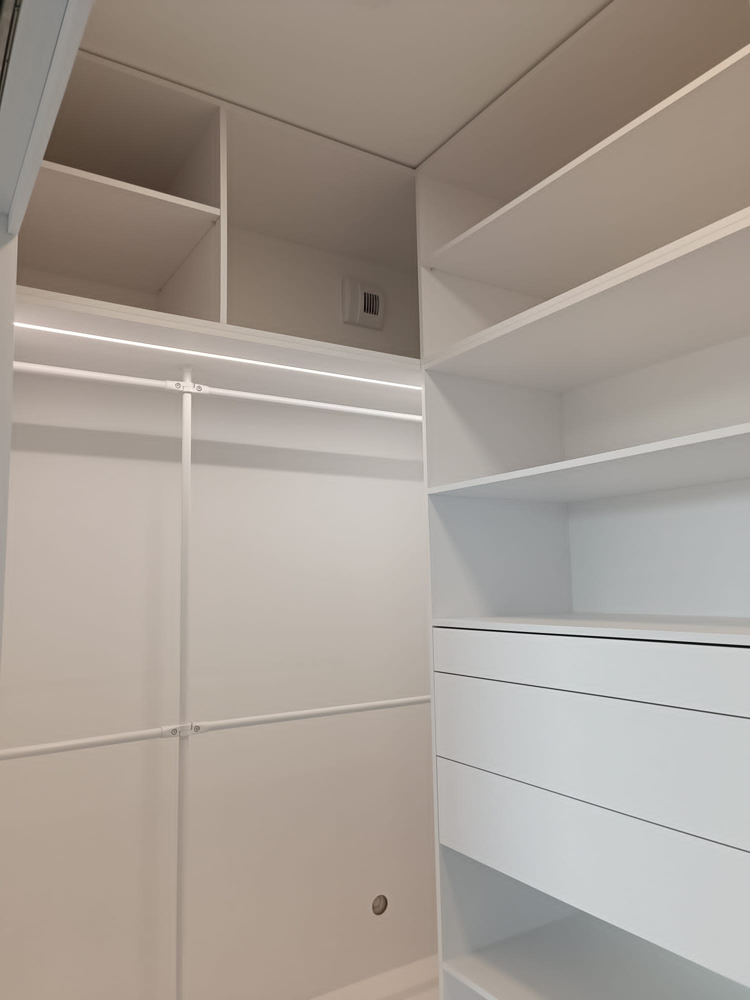Wnętrze białej szafy wnękowej z półkami i szufladami, oświetlenie LED w górnej części, widok z wnętrza szafy.