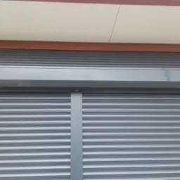 Szara, aluminiowa roleta zewnętrzna, zamknięta, widoczna od dołu z fragmentem elewacji i podsufitki.