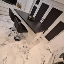 Nowoczesna kuchnia z marmurkową posadzką, czarnym blatem wyspy i oknami z plisami w kolorze antracytowym.