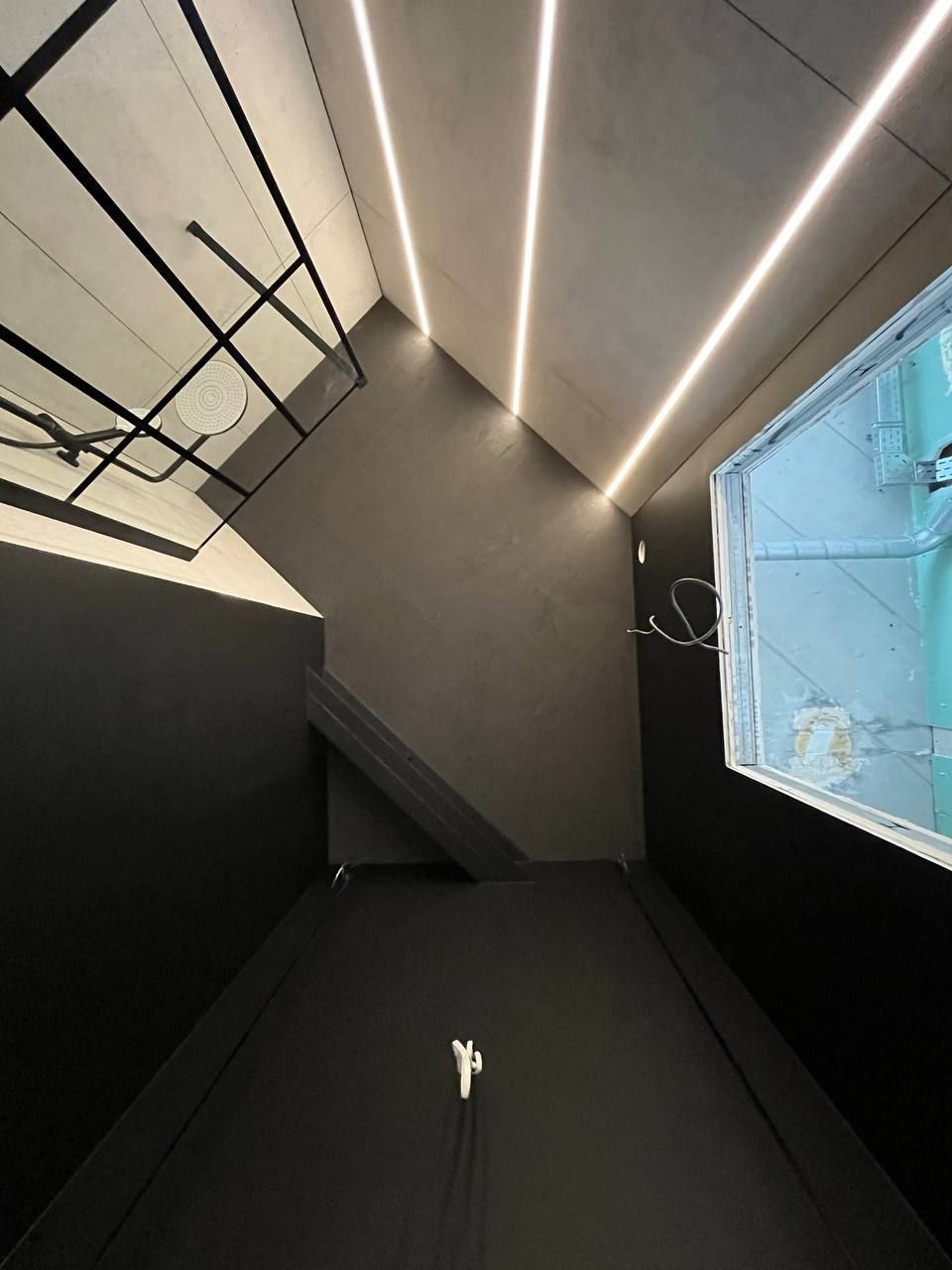 Nowoczesna łazienka z czarnymi ścianami, oświetleniem LED w suficie i przeszkloną kabiną prysznicową z deszczownicą, widziana z góry.