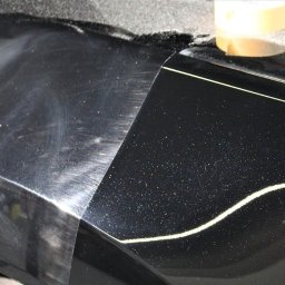 MYJNIA STARS CAR - Część karoserii czarnego, metalicznego samochodu, z widoczną różnicą w połysku i stanie lakieru przed i po polerowaniu, z taśmą maskującą oddzielającą obszary.