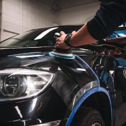 MYJNIA STARS CAR - Polerowanie lakieru czarnego samochodu przy użyciu polerki elektrycznej, z niebieską taśmą zabezpieczającą elementy.