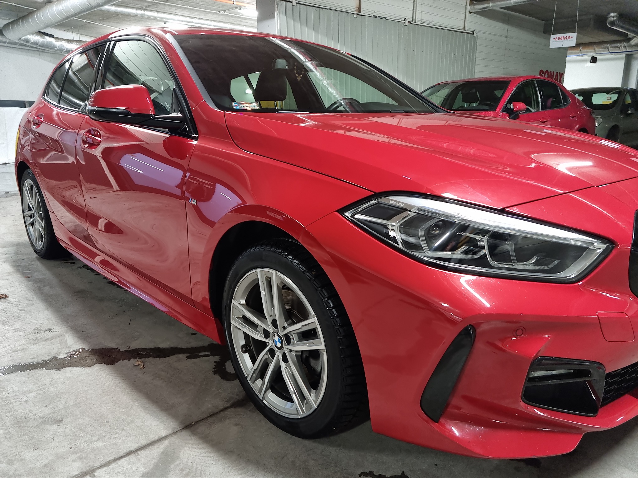 Czerwony samochód BMW serii 1 po umyciu, widoczne krople wody na podłożu, metalowe felgi, nowoczesne reflektory LED.