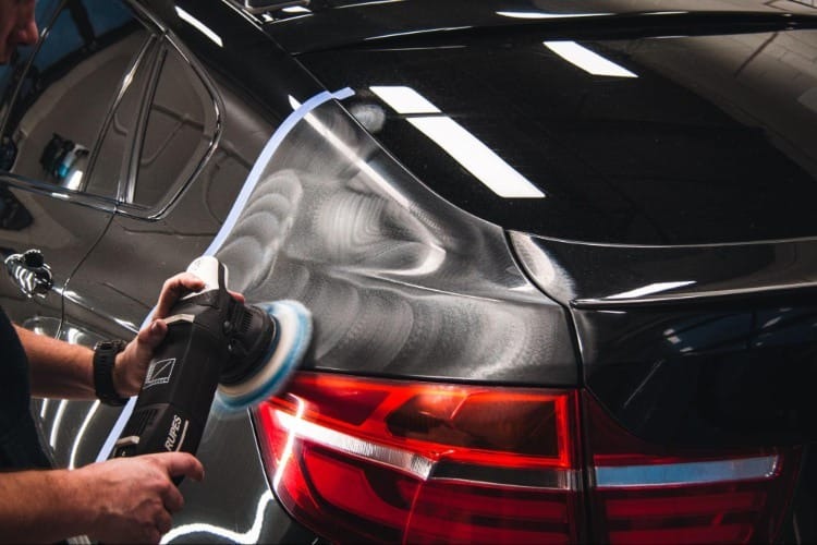 Polerowanie lakieru czarnego samochodu za pomocą polerki Rupes. Widoczne hologramy na lakierze przed polerowaniem. Taśma maskująca zabezpiecza krawędzie.