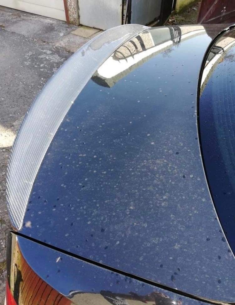 Bardzo brudny, czarny samochód z karbonowym spojlerem na bagażniku, widoczne liczne zacieki i osady na lakierze.