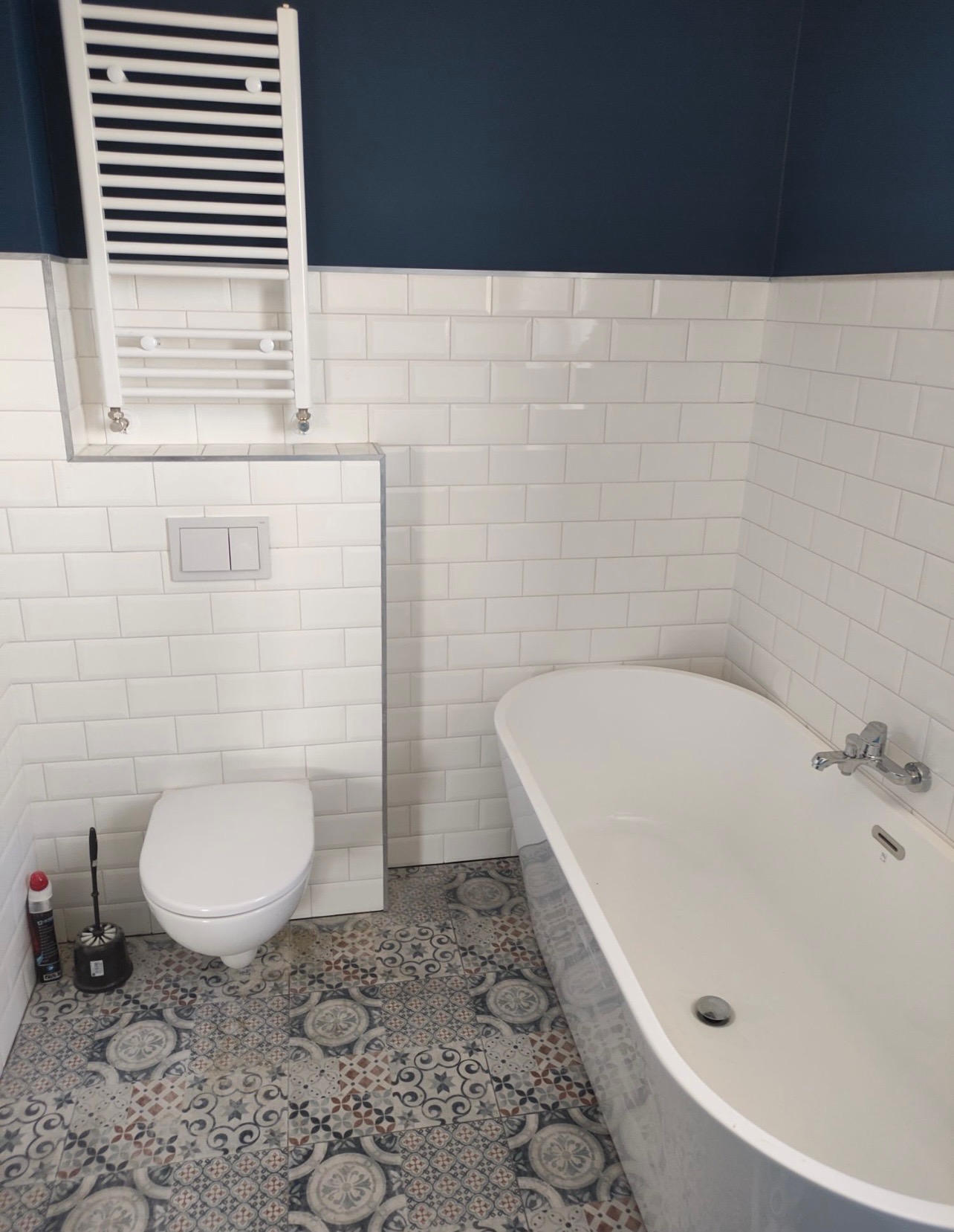 Nowoczesna łazienka z białą wanną wolnostojącą, toaletą podwieszaną, grzejnikiem drabinkowym i wzorzystą podłogą z płytek.