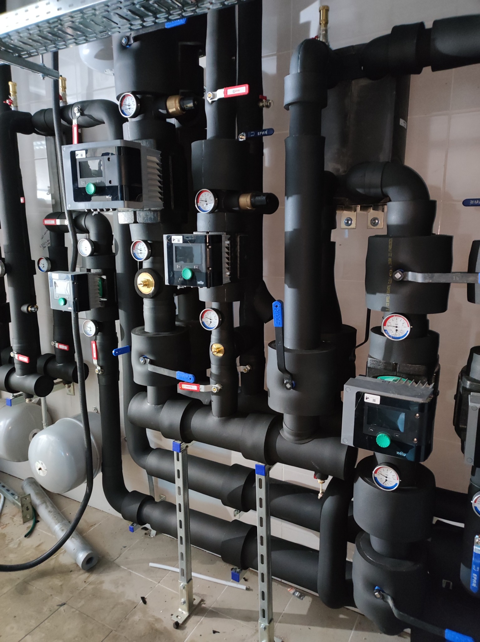 Kompleksowa instalacja rur grzewczych w izolacji z manometrami i zaworami, widoczne elementy sterujące Wilo i zbiorniki wyrównawcze.