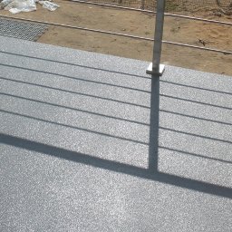 Perfect Coating System - Szara posadzka żywiczna na balkonie, widoczne cienie barierki i fragment otoczenia zewnętrznego z ziemią i workami.