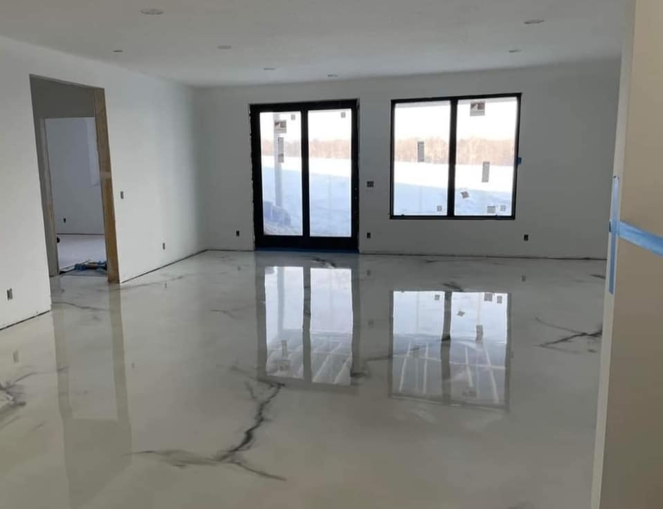 Błyszcząca, biała posadzka z szarymi żyłkami w przestronnym, jasnym pomieszczeniu z dużymi oknami i drzwiami balkonowymi, widoczne odbicia okien w podłodze.