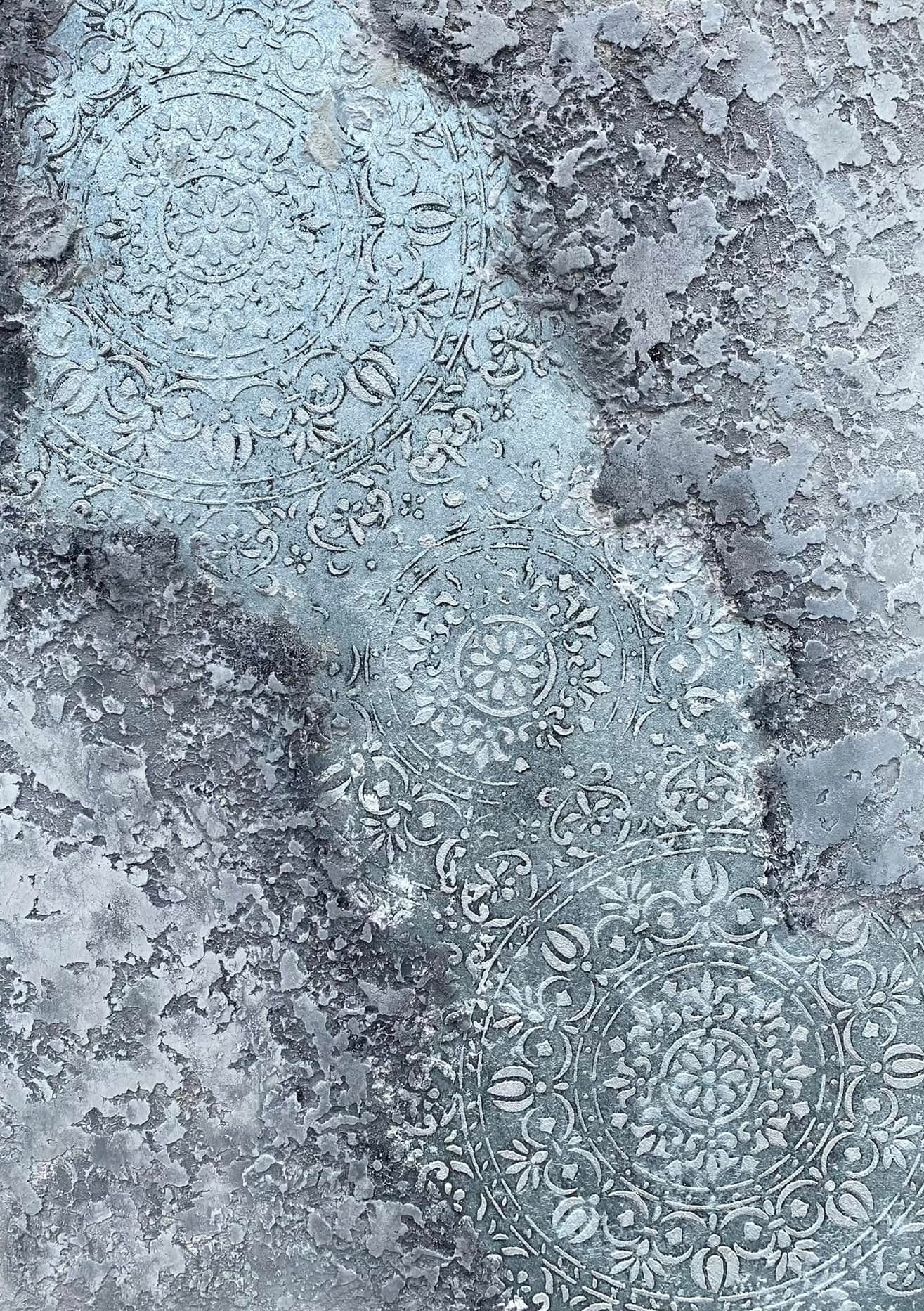 Szara, dekoracyjna powierzchnia z wytłoczonymi wzorami kwiatowymi w stylu mandali, przypominająca beton architektoniczny z efektem patyny.