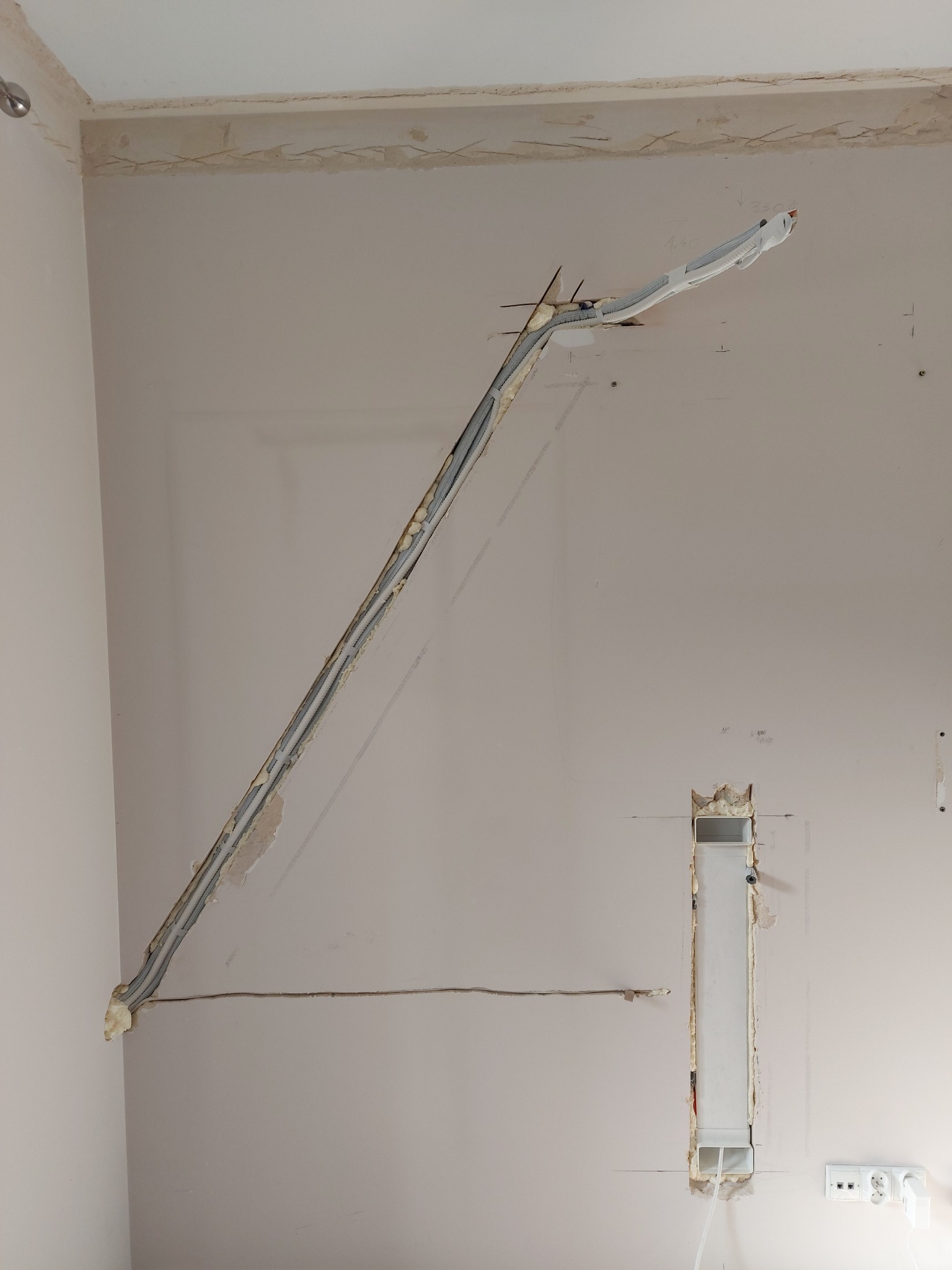 Instalacja przewodów wentylacyjnych w ścianie podczas remontu, widoczne wycięte bruzdy i pianka montażowa.