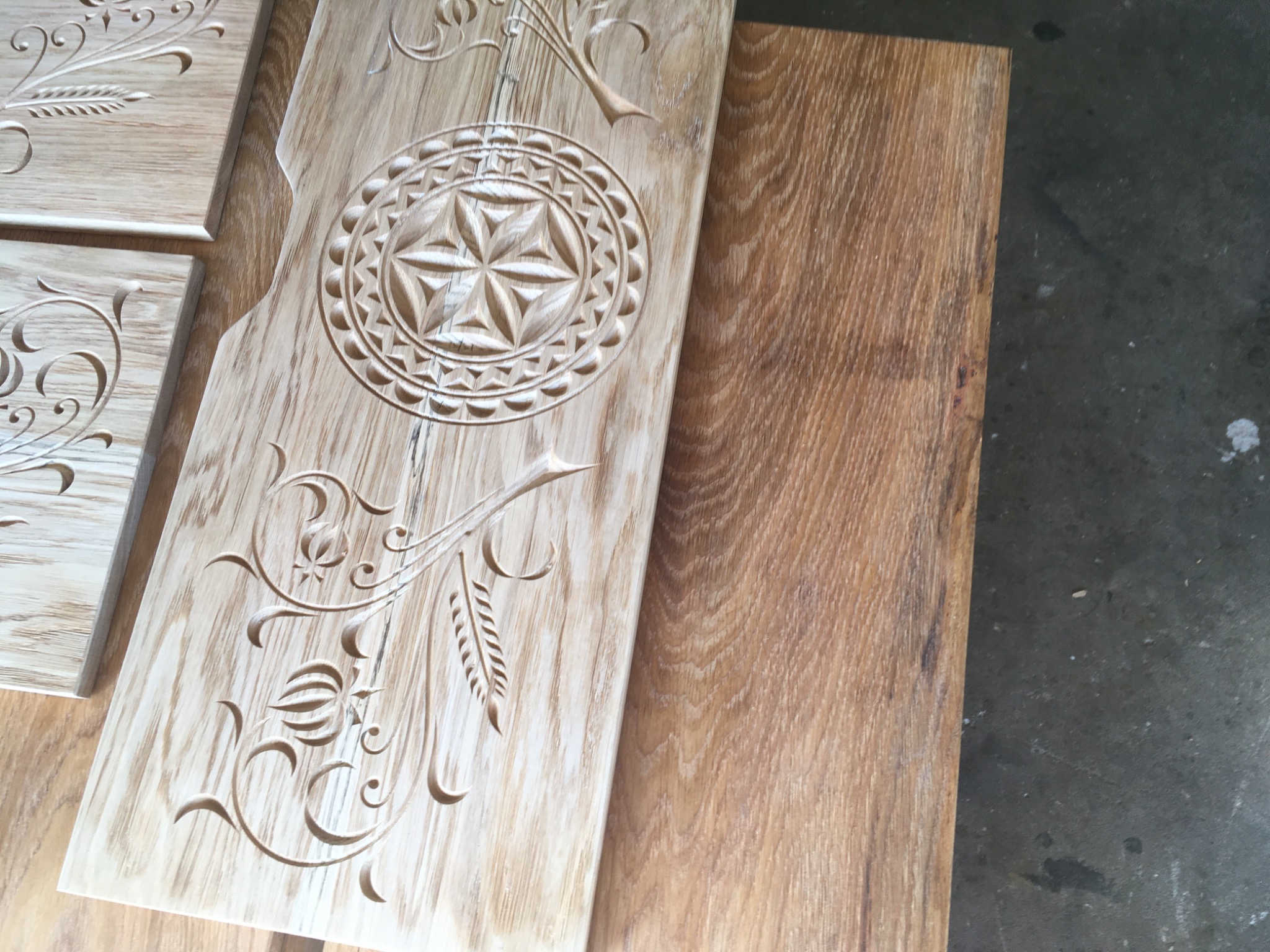 Drewniane panele z ręcznie rzeźbionymi ornamentami roślinnymi i geometrycznymi, leżące na blacie z jasnego drewna.