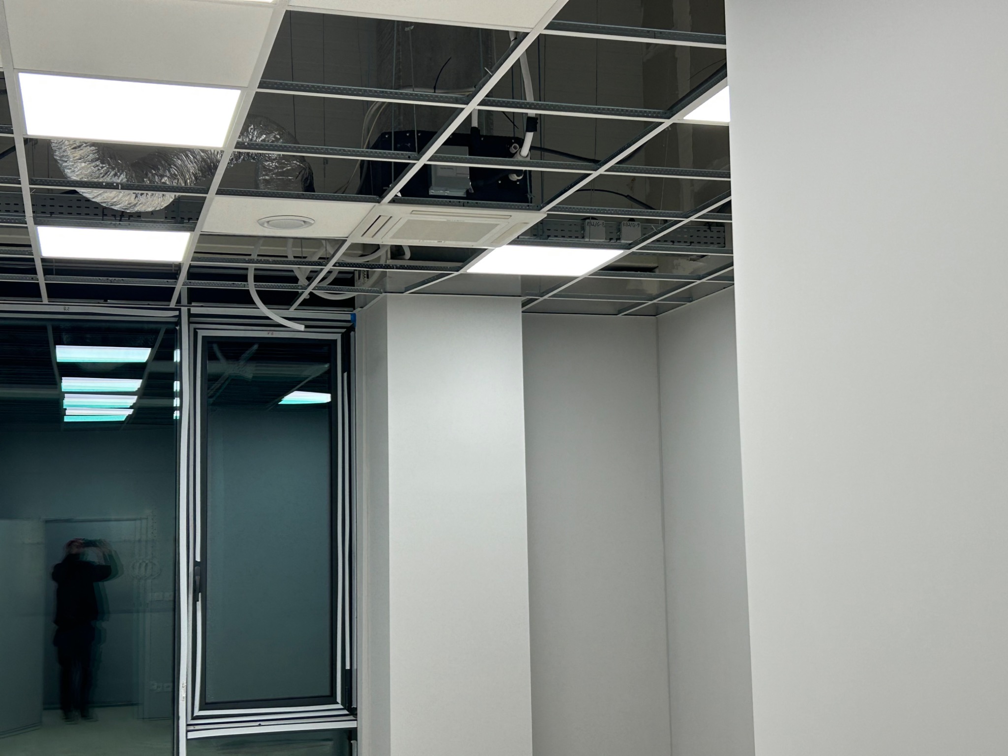 Sufit podwieszany z widoczną instalacją wentylacyjną, klimatyzacyjną i elektryczną w biurze, widoczne elementy konstrukcyjne i oświetlenie panelowe.