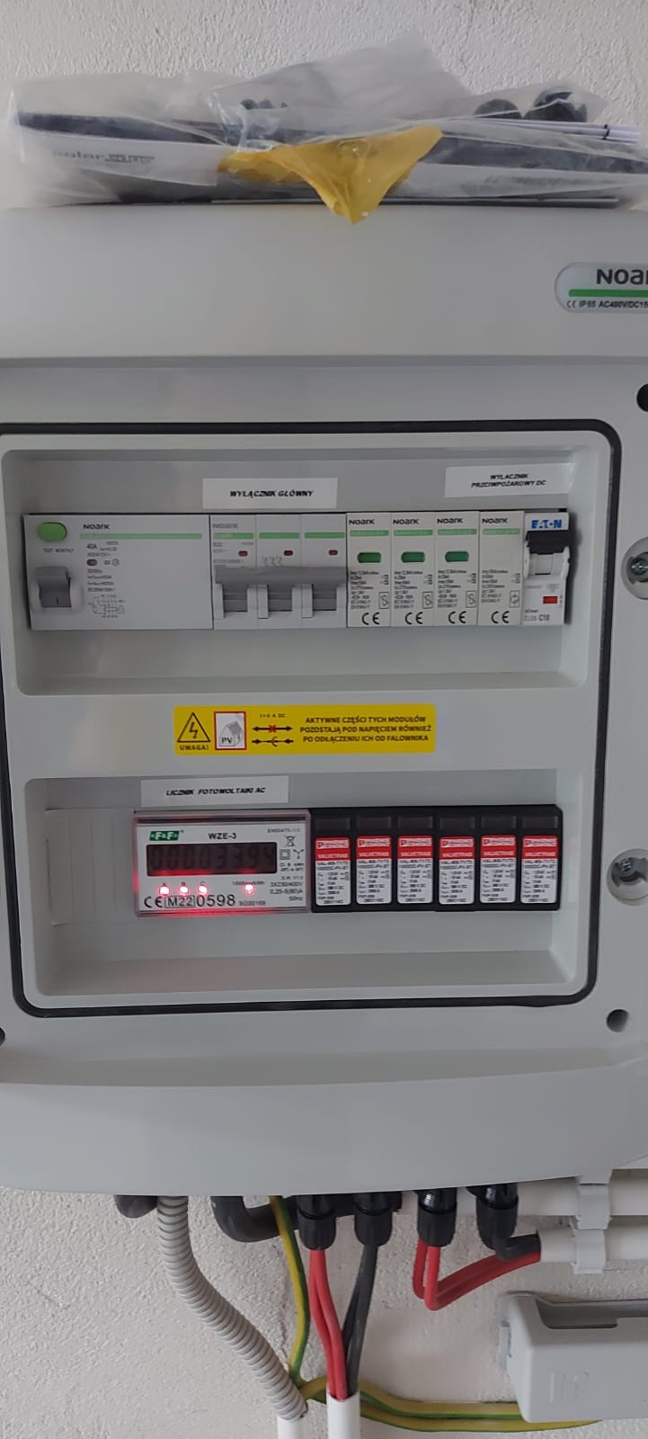 Rozdzielnica fotowoltaiczna z zainstalowanym licznikiem WZE-3, wyłącznikiem głównym i przeciwpożarowym DC, widoczne przewody zasilające.