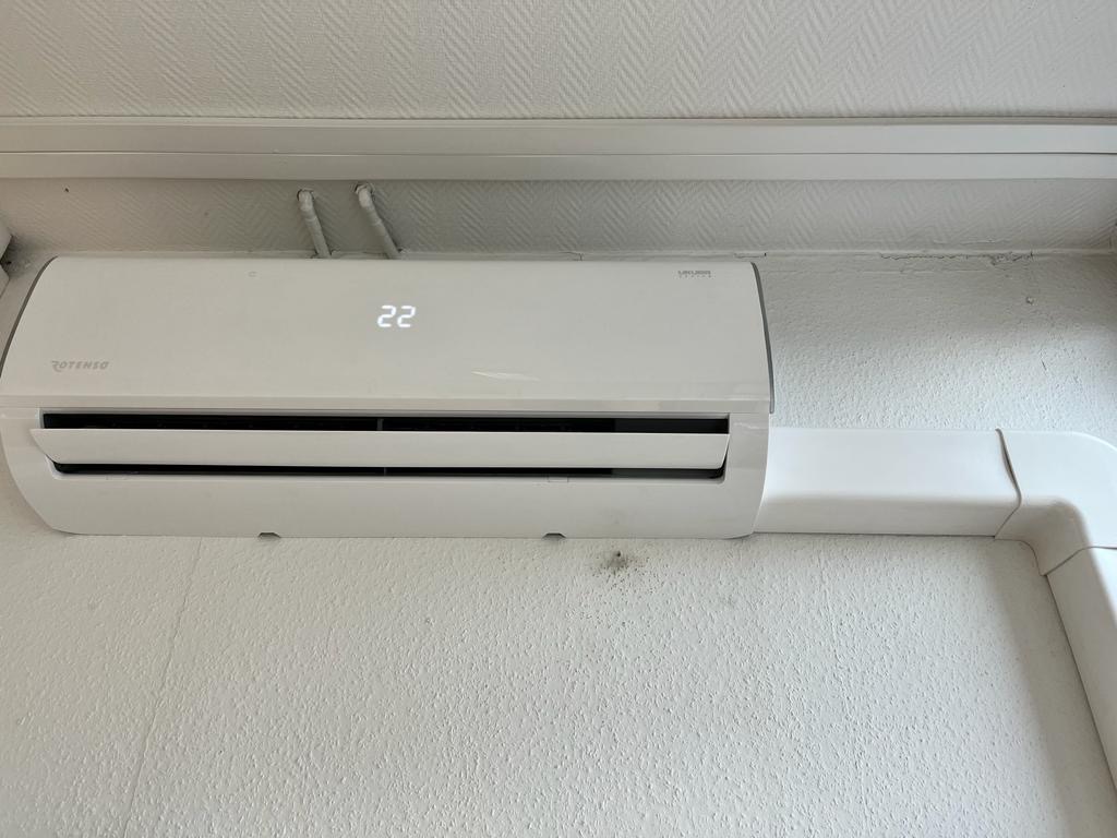 Biały klimatyzator Rotenso zamontowany na ścianie z widocznymi przewodami i wyświetlaczem wskazującym temperaturę 22 stopnie Celsjusza.