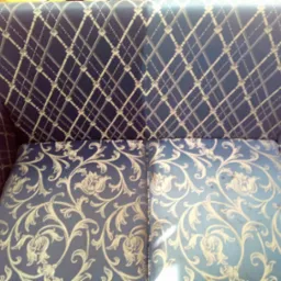 Fragment niebieskiej kanapy z dwoma różnymi wzorami tapicerki: kratka na oparciu i motyw roślinny na siedzisku. Widoczne plamy na jaśniejszej części siedziska.