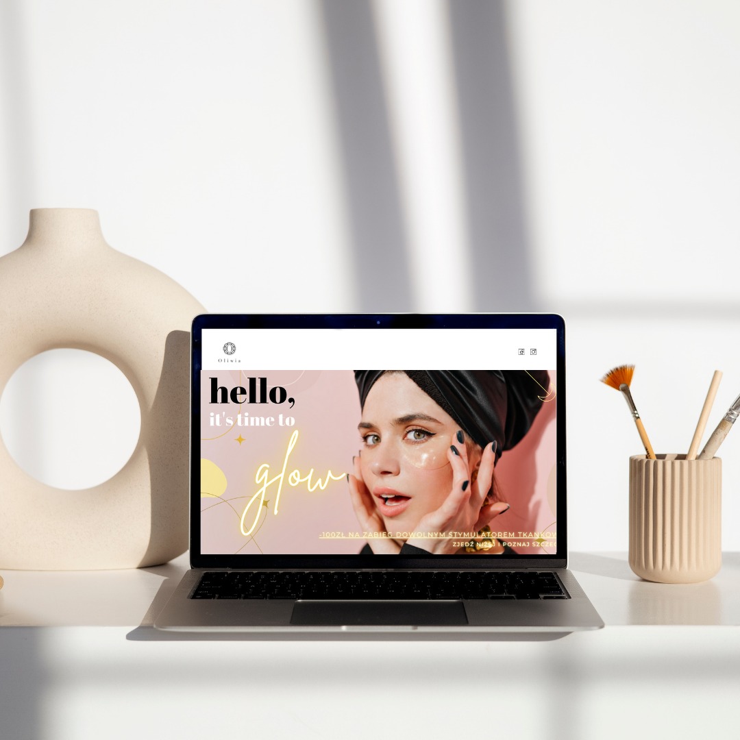 Laptop wyświetla stronę internetową z wizerunkiem kobiety z maseczkami pod oczami, obok wazon z otworem i pędzelki do makijażu, padające cienie tworzą abstrakcyjny wzór.