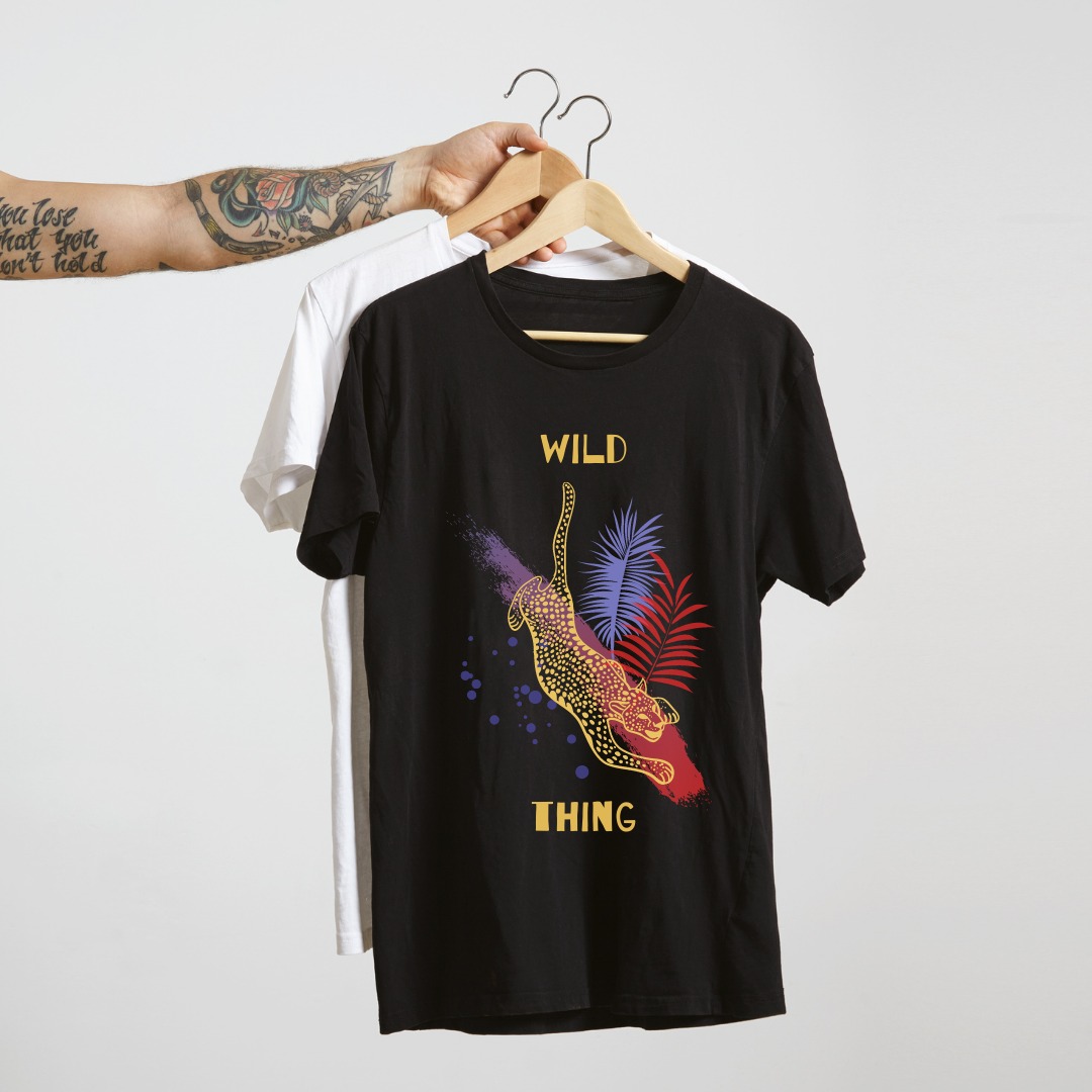 Czarna koszulka z nadrukiem przedstawiającym stylizowanego lamparta i tropikalne liście, wisząca na wieszaku obok białej koszulki, trzymana przez wytatuowaną rękę.