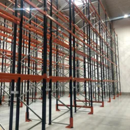 Puste, metalowe regały magazynowe w kolorze pomarańczowo-czarnym, widok z dołu, oświetlenie sufitowe.