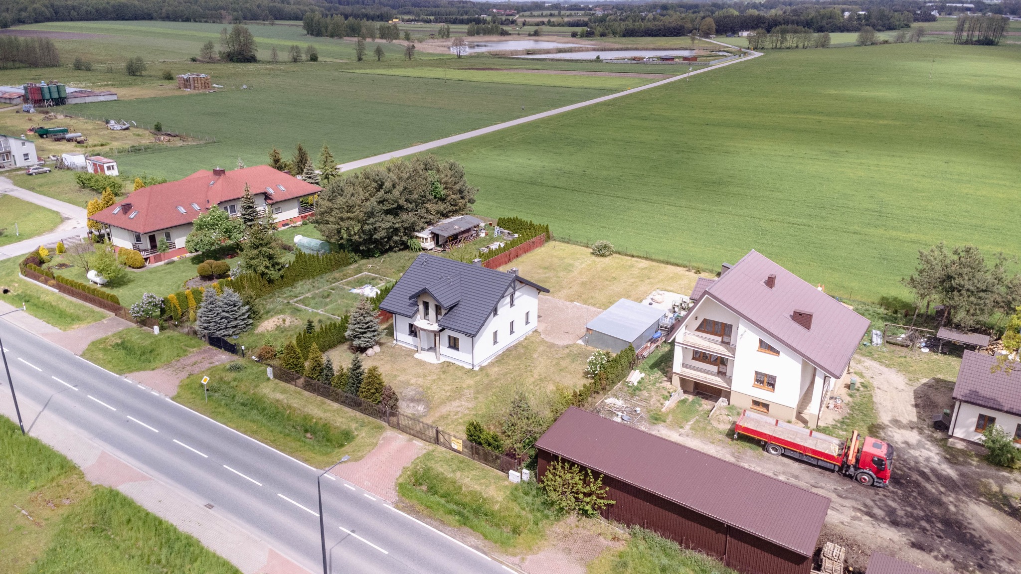 Widok z góry na kilka domów jednorodzinnych z ogrodami, z perspektywy drona, na tle zielonych pól i lasów.