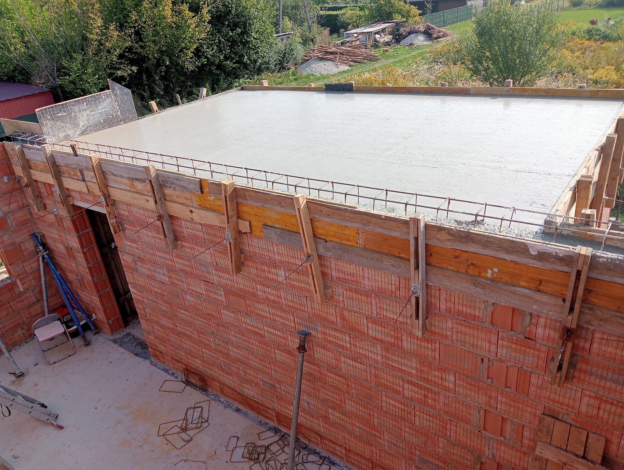 Wylany beton na stropie budynku w trakcie budowy, widoczne szalunki, zbrojenie oraz mur z pustaków ceramicznych.