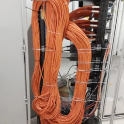 Pomarańczowe kable sieciowe uporządkowane w szafie serwerowej z metalowymi uchwytami i czarnymi elementami mocującymi.