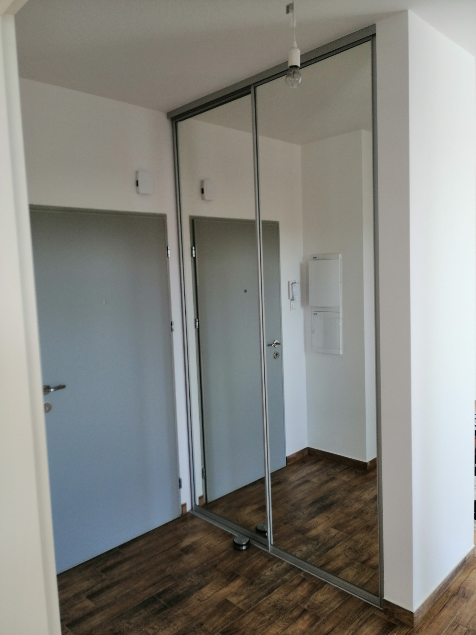 Nowoczesna szafa wnękowa z przesuwnymi drzwiami lustrzanymi, zamontowana w przedpokoju w Warszawie, z widocznym odbiciem drugiego pomieszczenia na drewnianej podłodze.