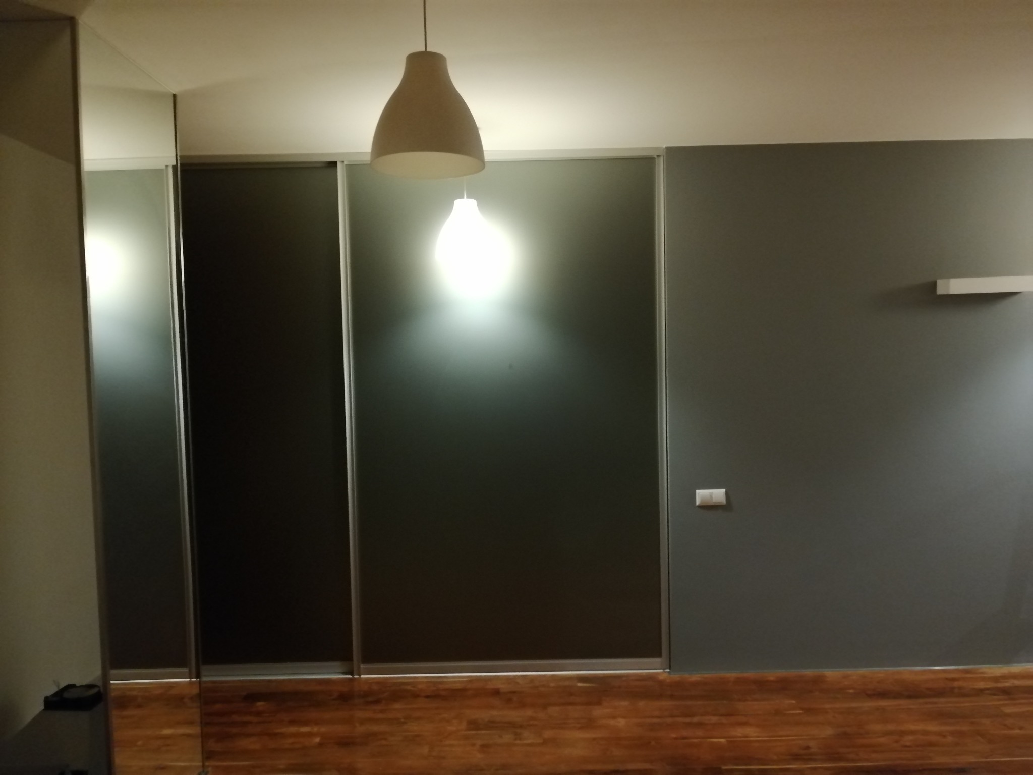 Szare drzwi przesuwne w szafie wnękowej z drewnianą podłogą i dwoma lampami wiszącymi.