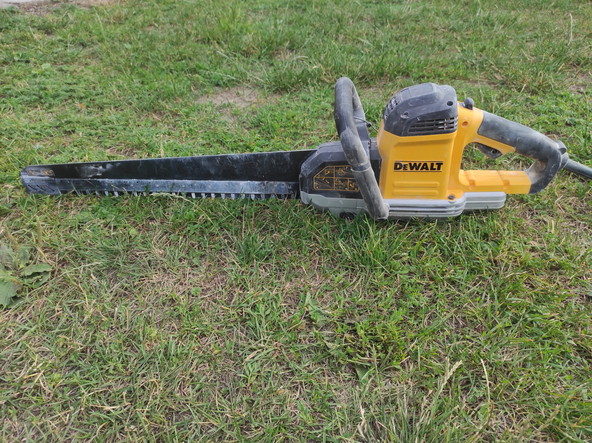 Elektryczna piła łańcuchowa DeWalt leżąca na trawie.