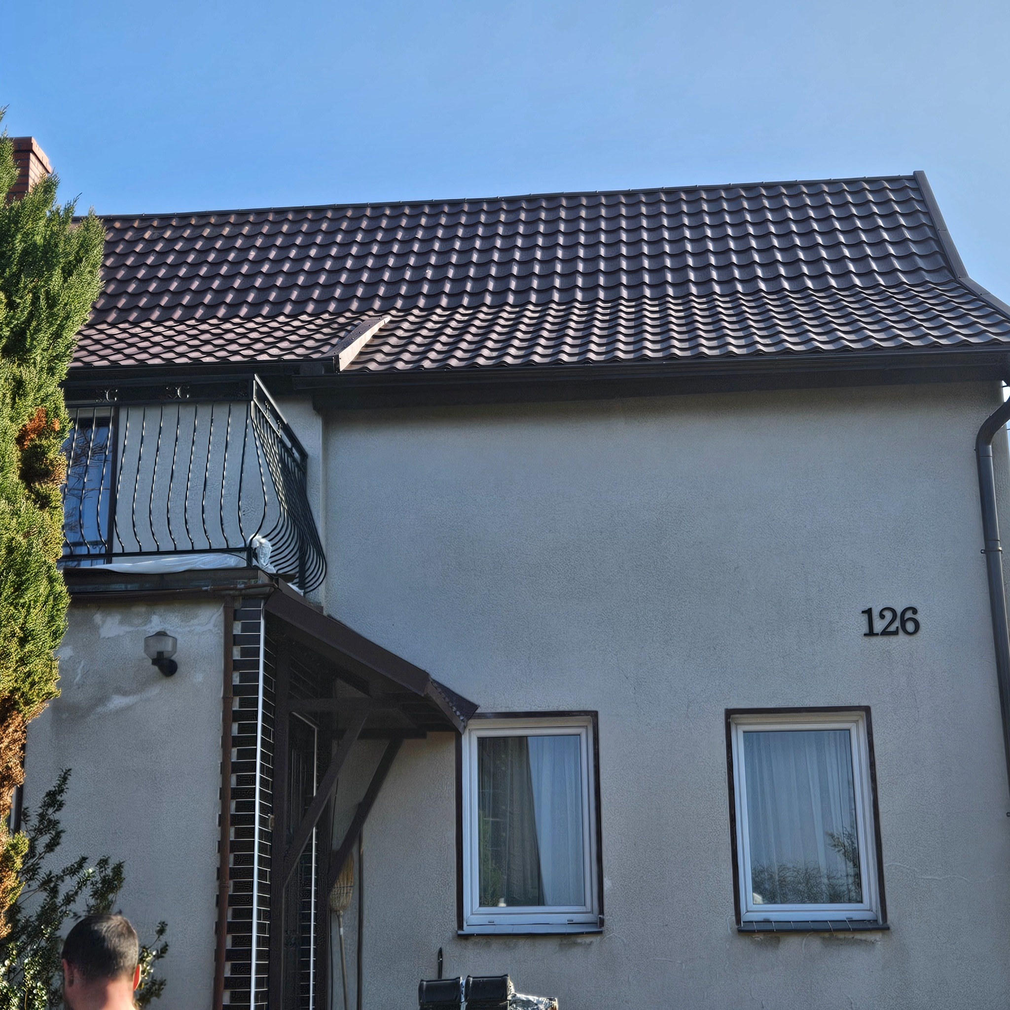 Dom jednorodzinny z nowym, brązowym dachem z dachówki ceramicznej, widoczny balkon z kutą balustradą i numer domu 126.
