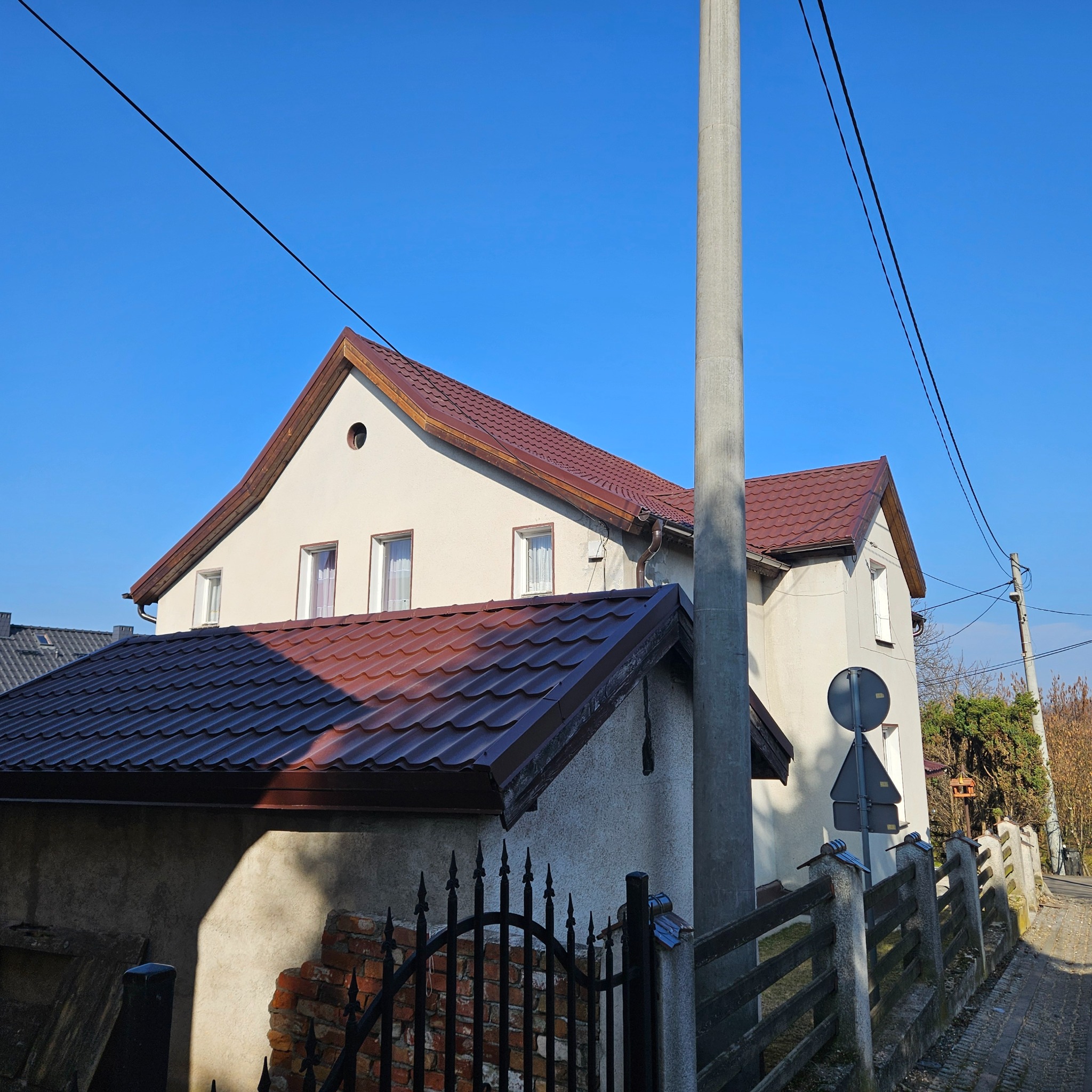 Dom jednorodzinny z nowym, brązowym dachem z blachodachówki, widok z ulicy, słoneczny dzień.