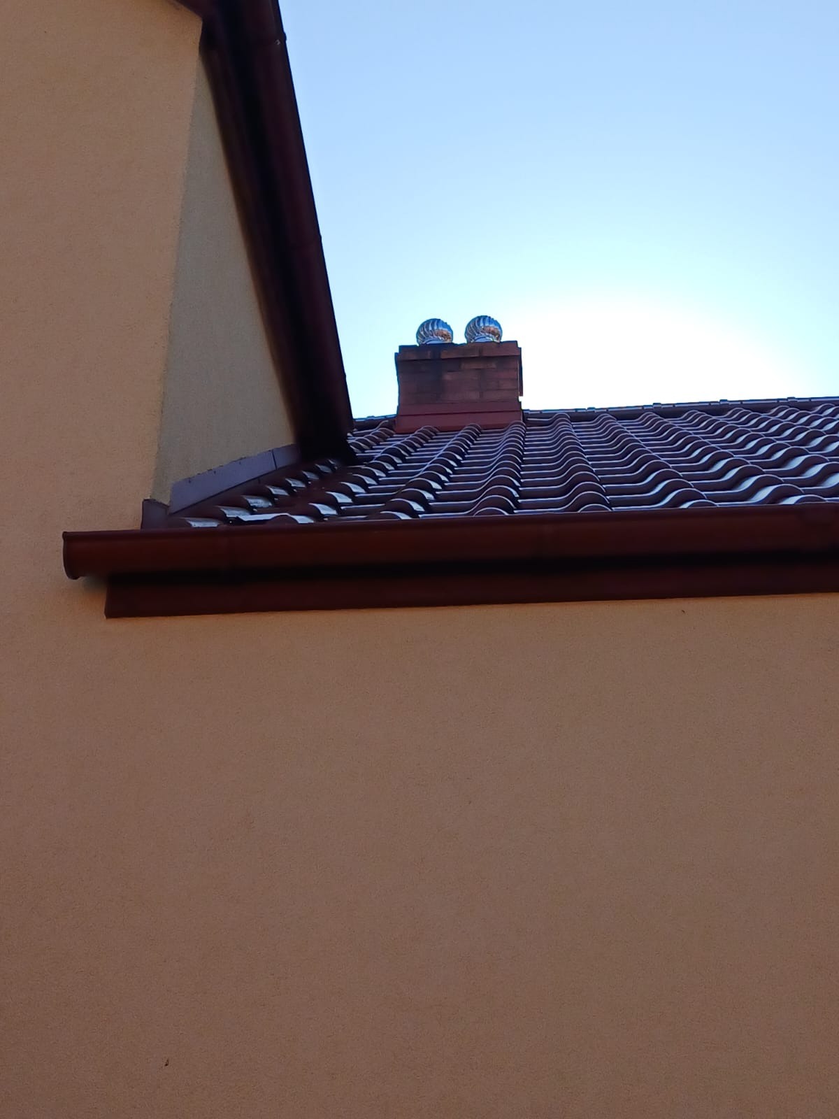 Czerwona dachówka ceramiczna na dachu domu z kominem i dwoma turbinami wiatrowymi, widok z dołu, jasne niebo.