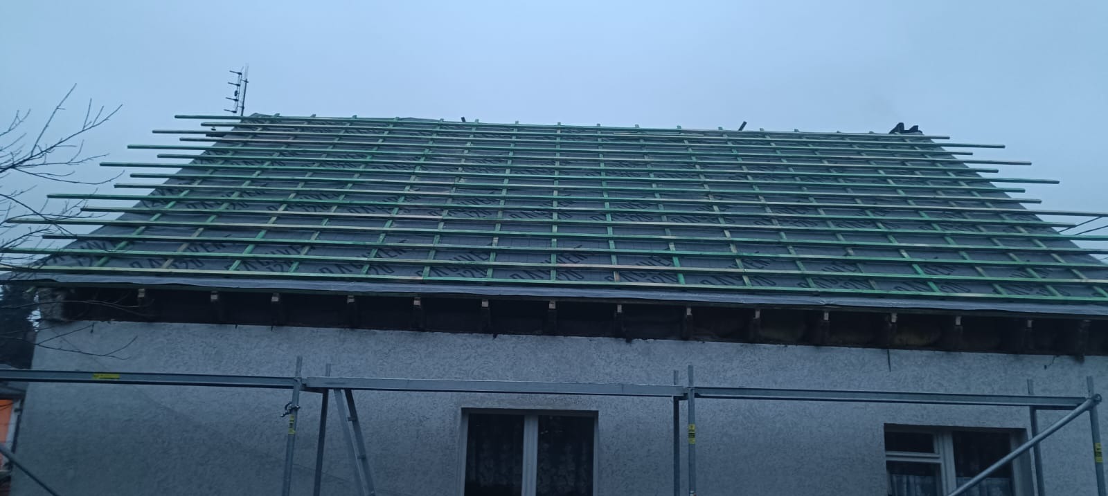 Konstrukcja dachu z łatami i membraną, widok z rusztowania. Etap przygotowania do pokrycia dachowego, pochmurne niebo w tle.