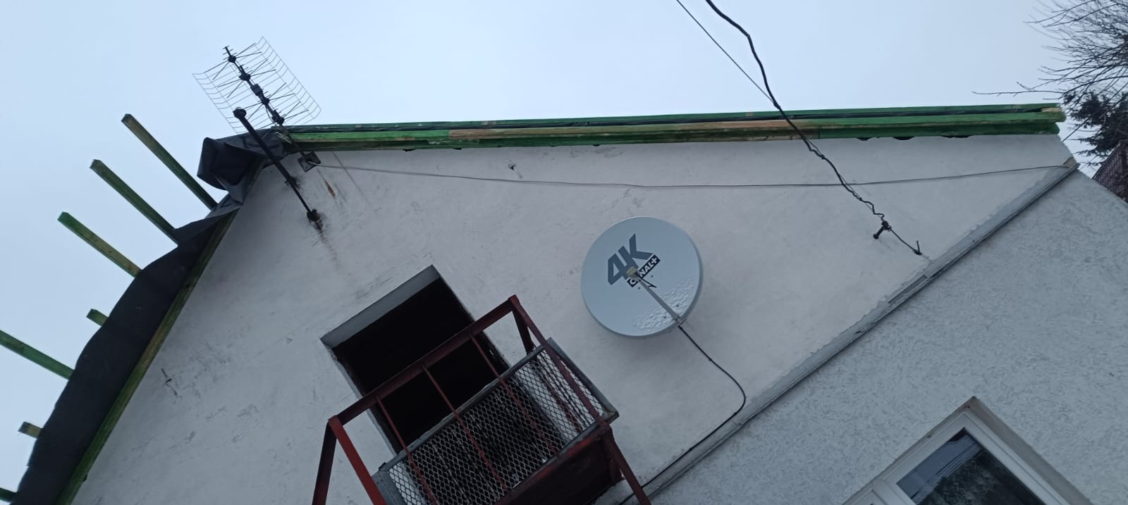 Demontaż dachu z widocznymi elementami konstrukcyjnymi i anteną satelitarną na ścianie budynku. Prace dekarskie w toku.