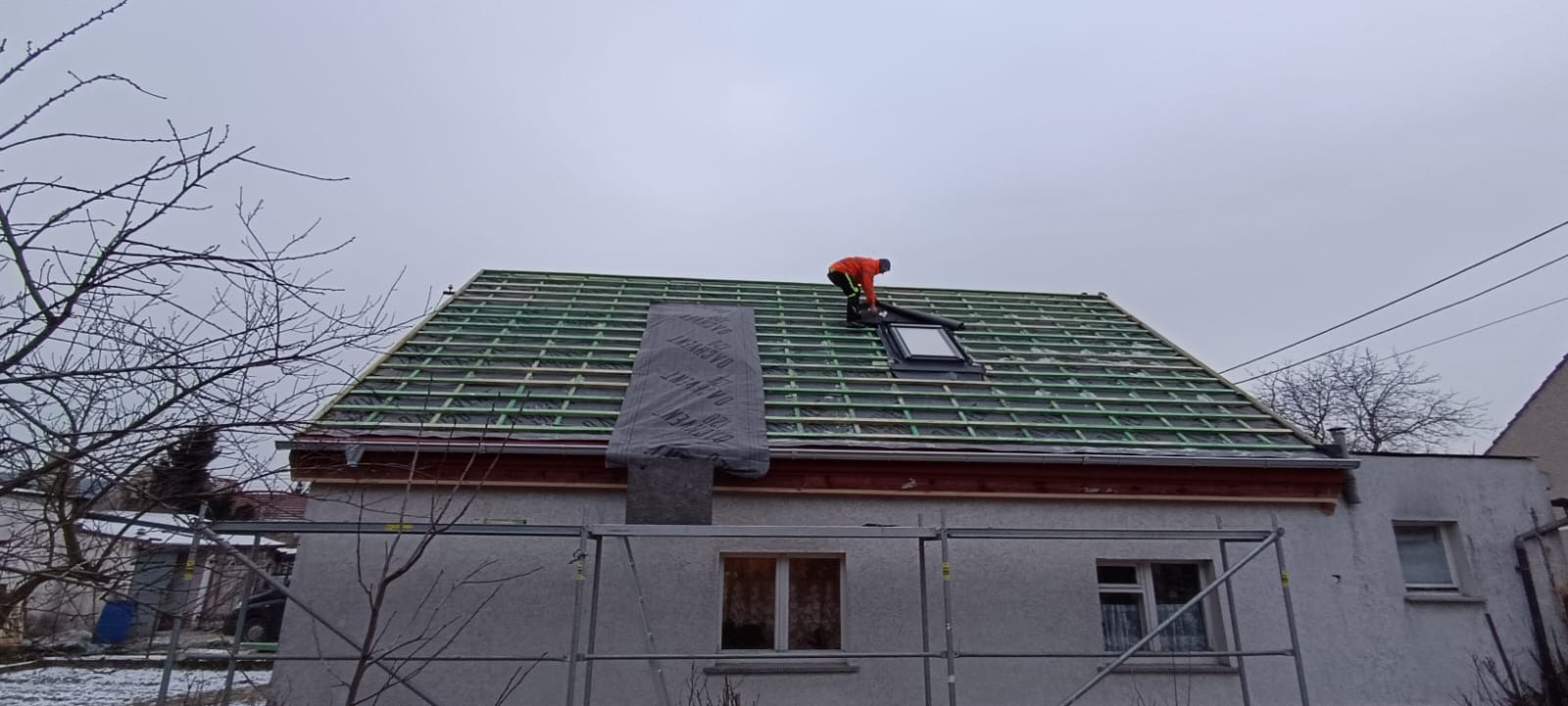 Montaż okna dachowego na przygotowanym dachu w Lubinie. Widoczna konstrukcja z łat i kontrłat, dekarz w pomarańczowej kurtce. Prace dekarskie w toku.