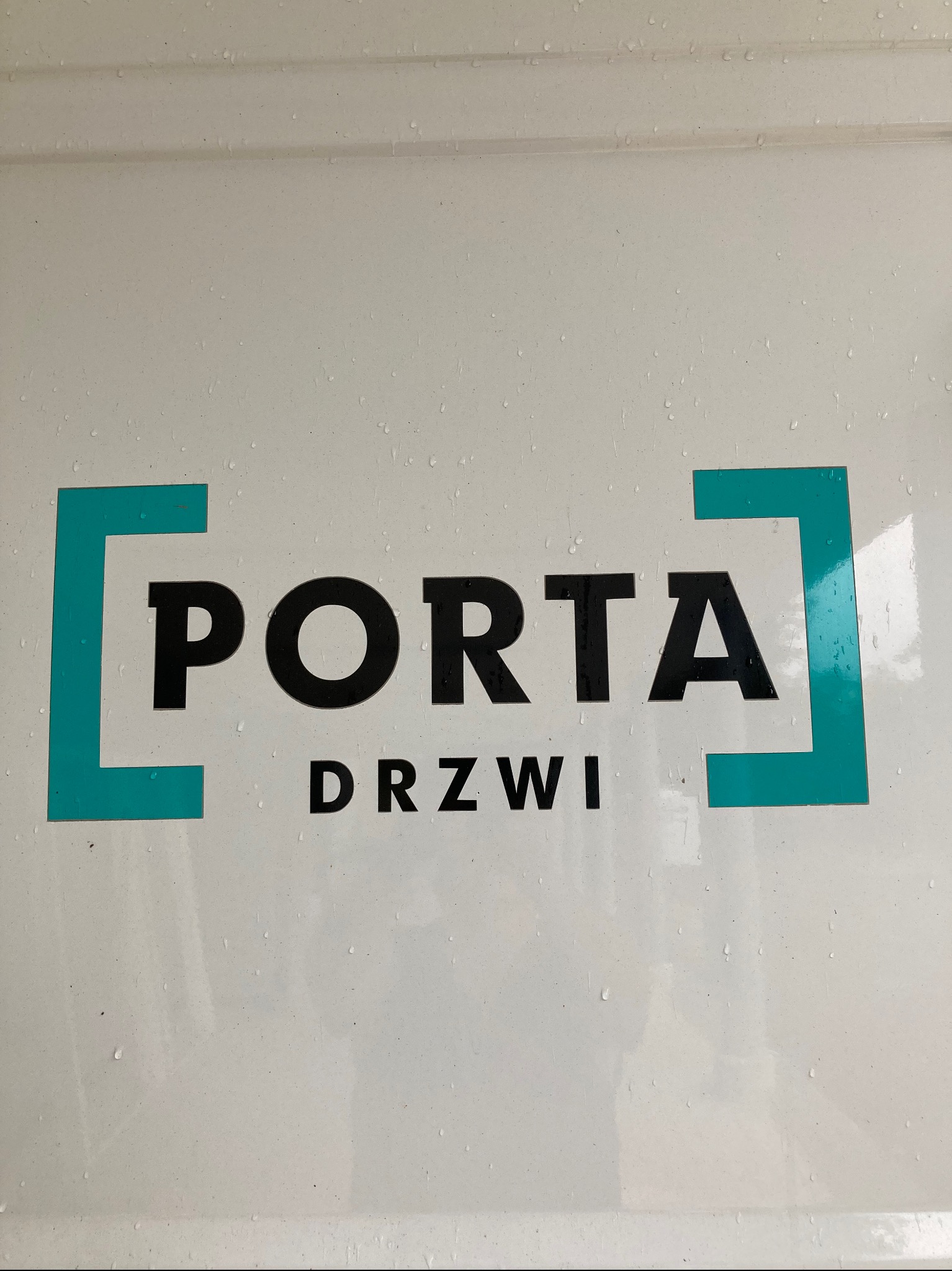 Logo firmy Porta Drzwi na jasnej powierzchni z widocznymi kroplami wody.