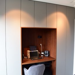 MODERN STUDIO W.FIRLEJ, M.FIRLEJ Spółka cywilna - Wnęka biurkowa z drewnianym blatem i szarą szafą wnękową, oświetlenie punktowe, laptop, tablet, głośniki i szare krzesło w sypialni.