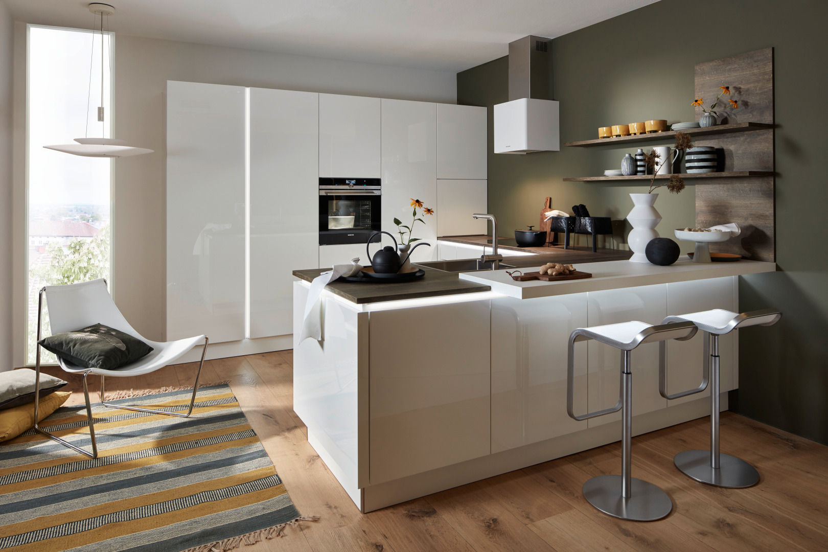 Nowoczesna kuchnia z białymi, lakierowanymi frontami, wyspą z podświetleniem LED, drewnianymi półkami na ścianie i krzesłami barowymi na metalowych nogach.