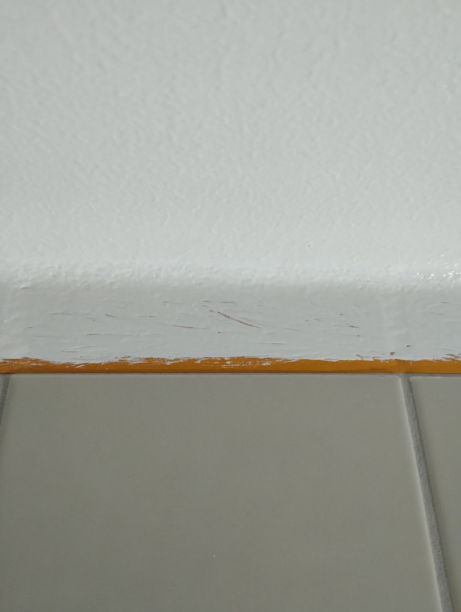 Świeżo pomalowana na biało ściana nad szarą glazurą zabezpieczona taśmą malarską, widoczne niedociągnięcia malarskie.