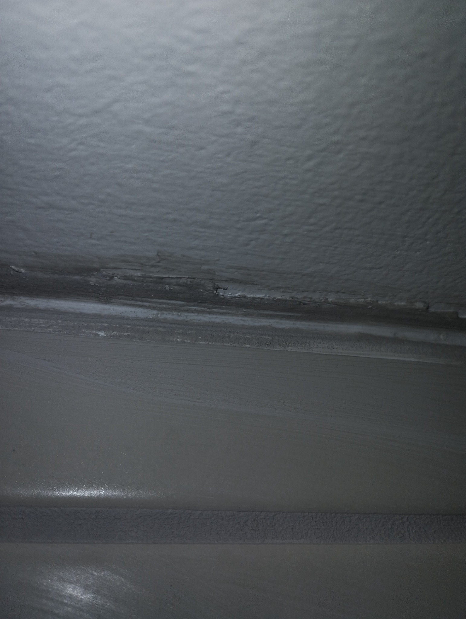 Szare, nierówno pomalowane połączenie ściany z sufitem, widoczne niedociągnięcia i pęknięcia farby.