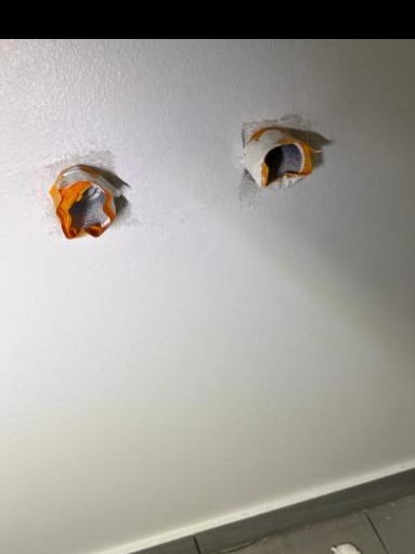 Przygotowane otwory w ścianie pod instalację elektryczną, zabezpieczone pomarańczową taśmą malarską przed malowaniem.