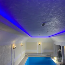 Wnętrze basenu z dekoracyjnym oświetleniem LED podsufitowym i ścianami wykończonymi w stylu klasycznym, widoczny pracownik w kombinezonie na tle kolumn.