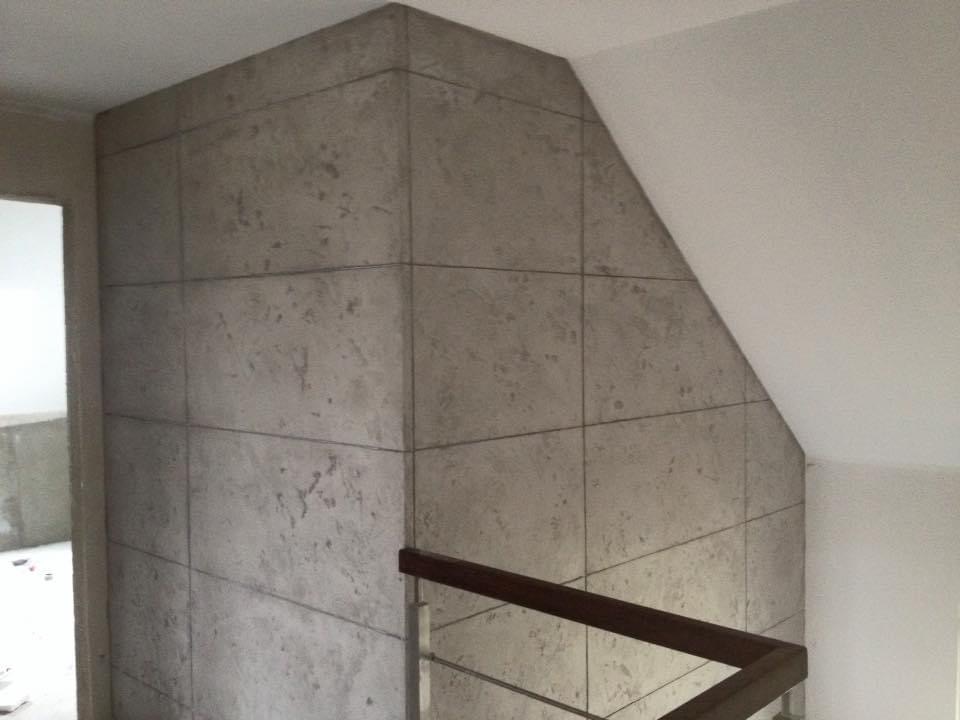 Ściana wewnętrzna wykończona panelami imitującymi beton architektoniczny, z widocznym fragmentem schodów z drewnianą balustradą w jasnym wnętrzu.