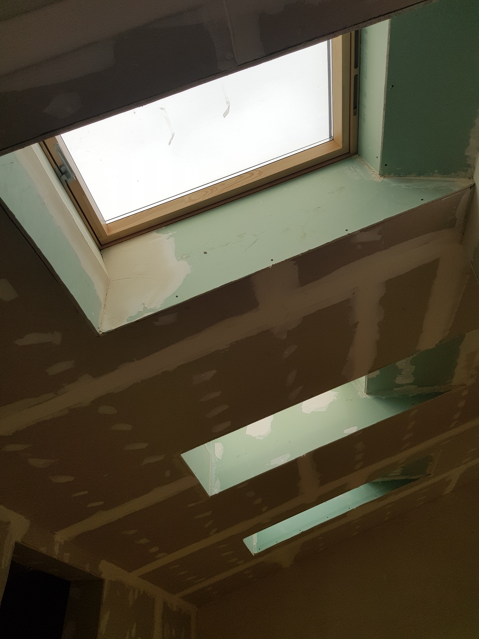 Sufit z płyt gipsowo-kartonowych z oknem dachowym i otworami na oświetlenie, w trakcie szpachlowania łączeń.