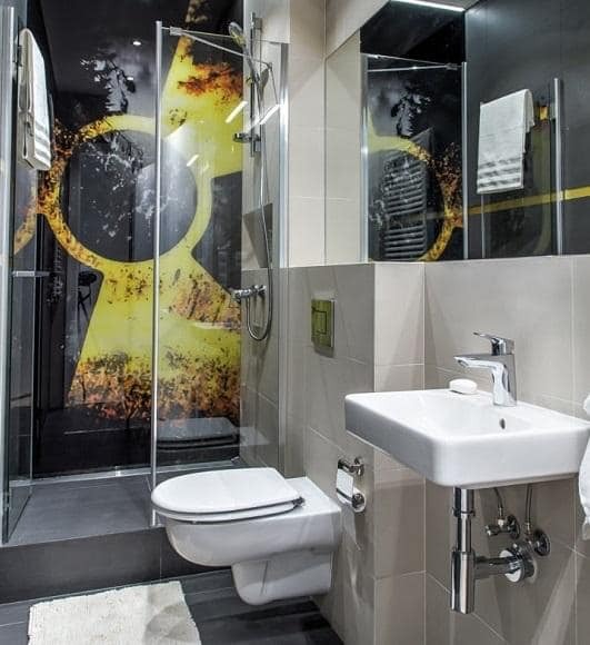 Nowoczesna łazienka z kabiną prysznicową z grafiką, podwieszaną toaletą i umywalką na tle szarych płytek.