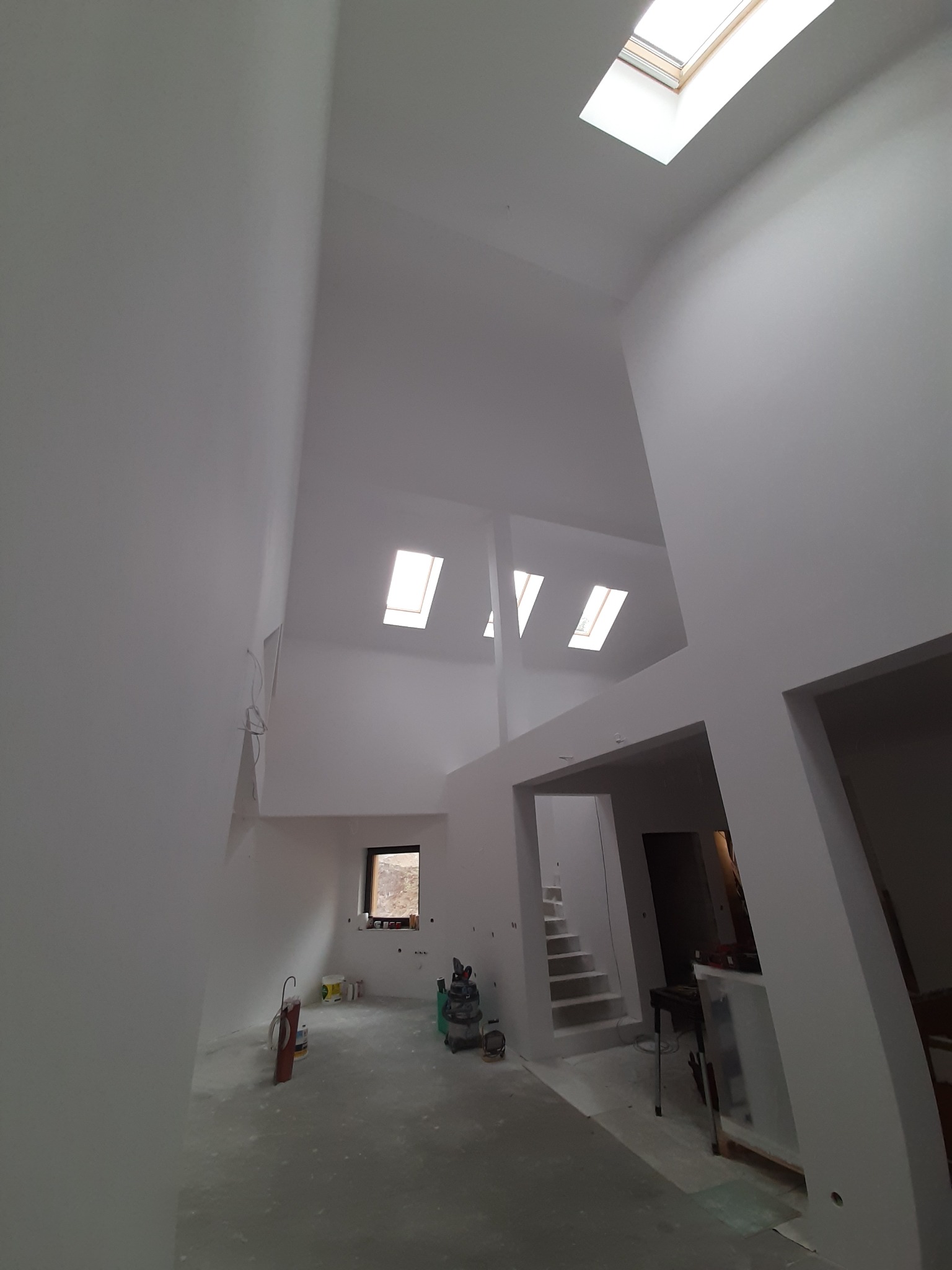 Wnętrze dwupoziomowego pomieszczenia z wysokim sufitem i oknami dachowymi po świeżym malowaniu na biało, widoczne ślady po pracach wykończeniowych, narzędzia i farby w tle.