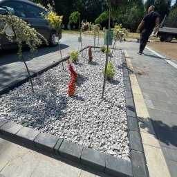 WAVE-LOG SP zoo - Obrzeża z kostki brukowej okalają rabatę z kamykami i roślinami. Ułożona nawierzchnia z kostki w odcieniach szarości. Prace wykończeniowe w ogrodzie, widoczny pracownik.