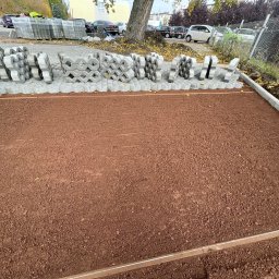 WAVE-LOG SP zoo - Przygotowany teren pod ażurowe płyty betonowe. W tle zapakowane płyty i zaparkowane samochody. Widok z góry na brązową ziemię i szare płyty.