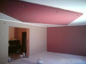 Pomalowane wnętrze pokoju z podwieszonym sufitem w kolorze burgundowym z punktowym oświetleniem, ściany w odcieniach beżu i bordo, widoczne przygotowania do prac wykończeniowych.